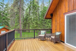 A wooden deck with two wicker chairs and a small table, overlooking a forested area. - 2BR cabin with patio & grill - close to the lake (Ronald)