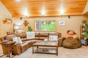 A cozy living room with a brown leather sectional sofa, a wooden coffee table, and a large stuffed animal. - 2BR cabin with patio & grill - close to the lake (Ronald)