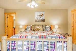 A bedroom with a bed, wooden headboard, two bedside tables, a ceiling fan, and a wall-mounted painting of a moose. - 2BR cabin with patio & grill - close to the lake (Ronald)