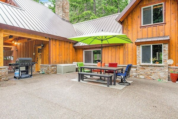A wooden cabin with a patio area featuring a grill, a table with chairs, and a green umbrella. - 2BR cabin with patio & grill - close to the lake (Ronald)