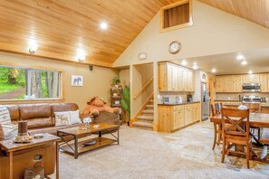 A cozy living room with a sofa, coffee table, and a fireplace. There is a kitchen area with wooden cabinets and a dining table. - 2BR cabin with patio & grill - close to the lake (Ronald)