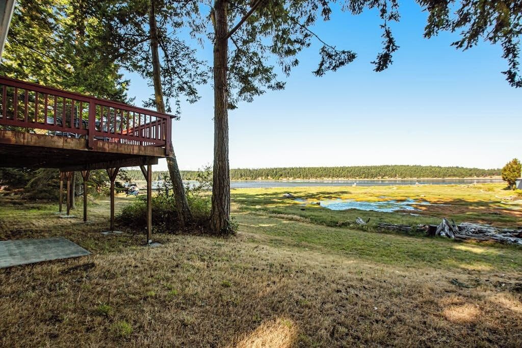 A wooden deck with railings overlooking a grassy area with trees and a distant view of a body of water.