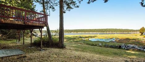 A wooden deck with railings overlooking a grassy area with trees and a distant view of a body of water.