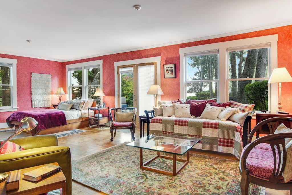 A room with a bed, a sofa, a coffee table, and a chair. There are windows and a door.