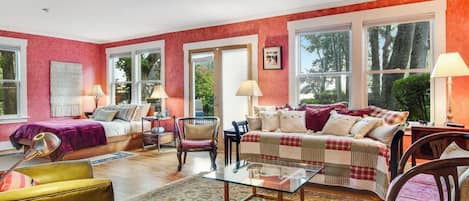 A room with a bed, a sofa, a coffee table, and a chair. There are windows and a door.