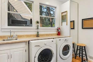 A laundry room with two washing machines, a sink, and a window with a view of trees.