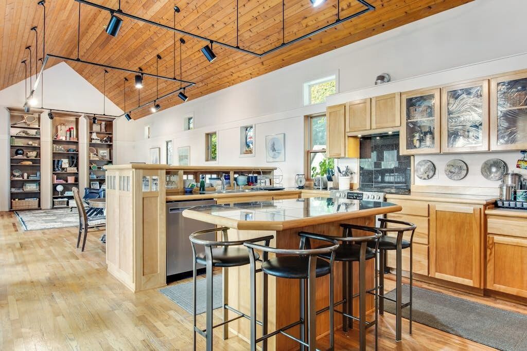 A modern kitchen with a central island, bar stools, wooden cabinets, and pendant lighting.