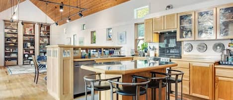A modern kitchen with a central island, bar stools, wooden cabinets, and pendant lighting.
