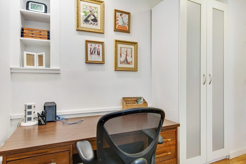 Une pièce comprenant un bureau en bois, une chaise, une armoire et quatre tableaux encadrés accrochés au mur.
