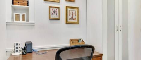 A room with a wooden desk, a chair, a wardrobe, and four framed pictures on the wall.