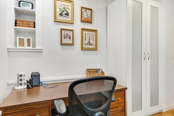 A room with a wooden desk, a chair, a wardrobe, and four framed pictures on the wall.