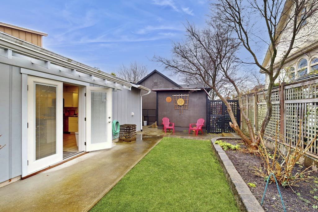 Un jardin arrière d’une maison, avec une pelouse, deux chaises roses, un abri de jardin et une clôture.