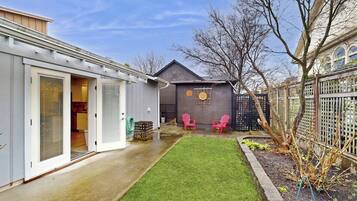 Un jardin arrière d’une maison, avec une pelouse, deux chaises roses, un abri de jardin et une clôture.