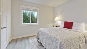 Een slaapkamer met een bed, een raam, een nachtkastje en een lamp.