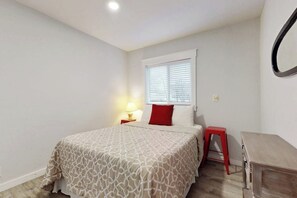 Ein Schlafzimmer mit einem Bett, einem Nachttisch, einem roten Hocker und einem Holztisch.
