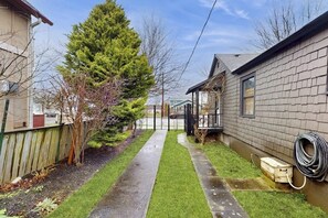 A residential property with a paved driveway, a lawn, a wooden fence, and a house with a brick exterior. - Cozy 2BR - Fireplace - Patio - Washer Dryer (Anacortes)