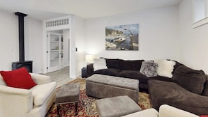 Een woonkamer met een open haard, een zithoek, een vloerkleed en een schilderij aan de muur.