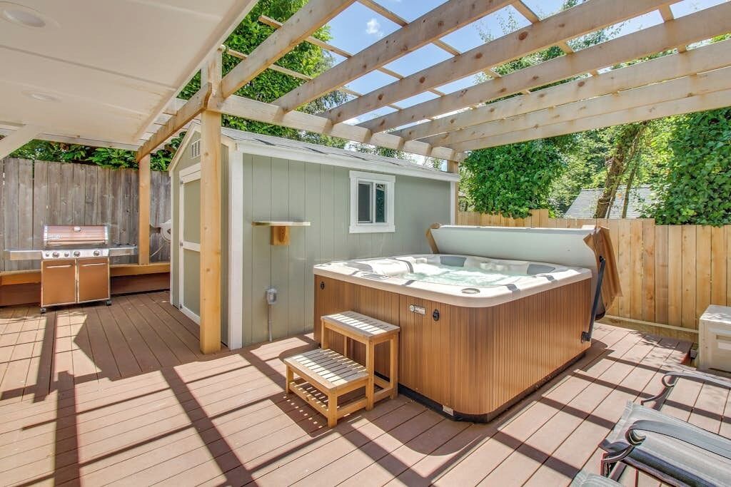 Una terraza de madera con un jacuzzi, una parrilla y un cobertizo pequeño.