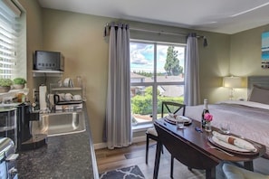 A hotel room with a bed, a dining table, a TV, a sink, and a window with curtains. - Cozy Studio Lakeview - Deck - NoKitchen- Shared Hot Tub (Mercer Island)