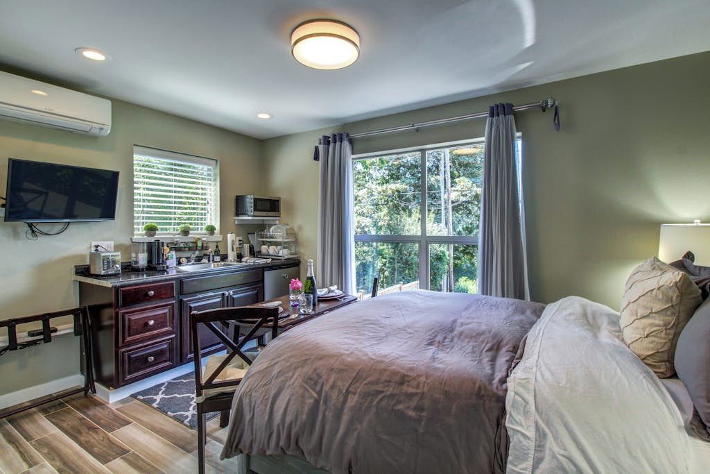 A bedroom with a bed, a desk with a chair, a television, and a window with curtains.