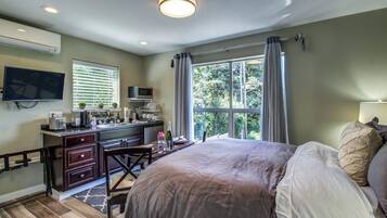A bedroom with a bed, a desk with a chair, a television, and a window with curtains.