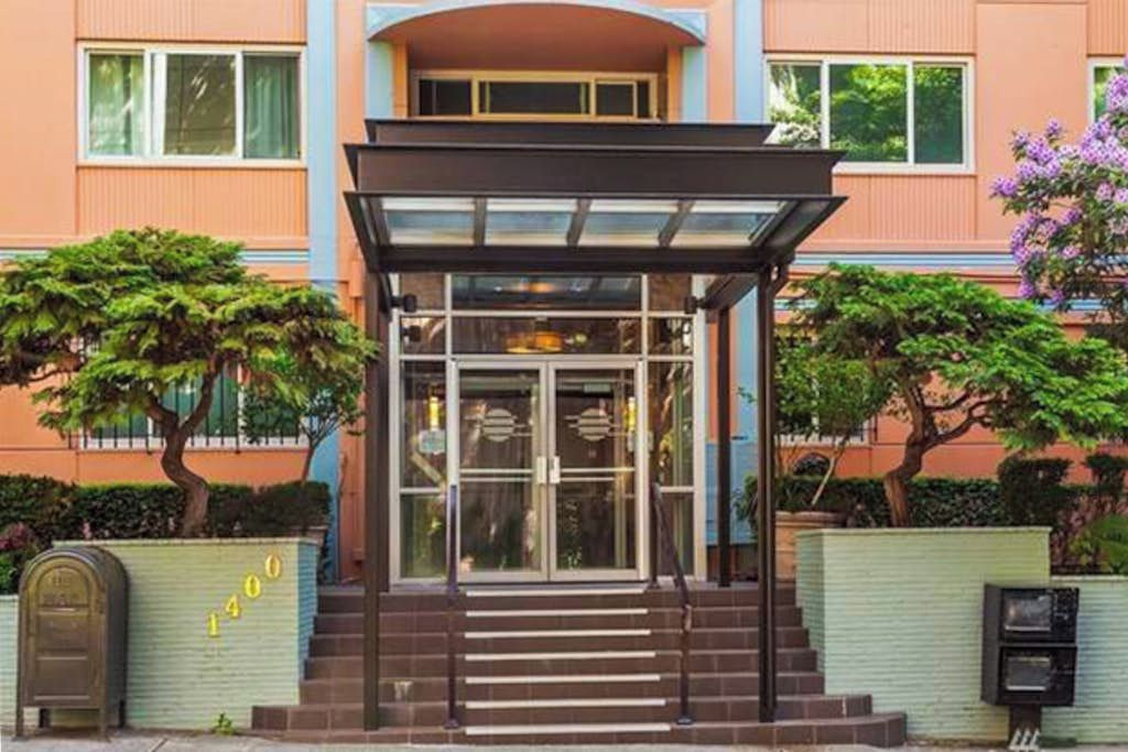 A hotel entrance with a glass door, a covered waiting area, and a staircase leading up to the entrance.