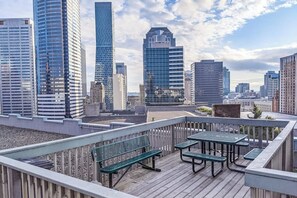 Eine Dachterrasse mit Holzdeck, Metallbänken und Blick auf einen Stadt-Horizont mit modernen Gebäuden.