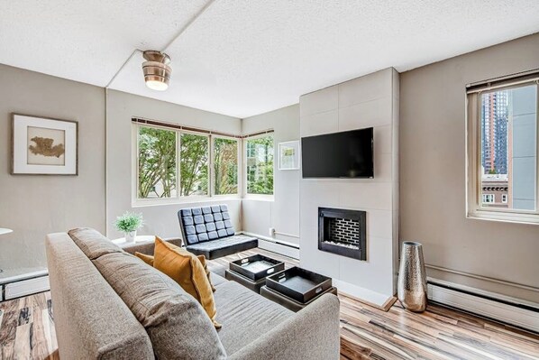 A modern living room with a sofa, a flat-screen TV, a fireplace, and large windows. - City 1BR Washington State Conv. Center 12th-Floor (Seattle)