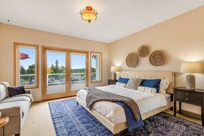 A bedroom with a large bed, a nightstand, a chair, and a view through a sliding door.