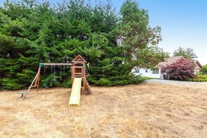 A playground with a slide and swings, surrounded by trees and a house.