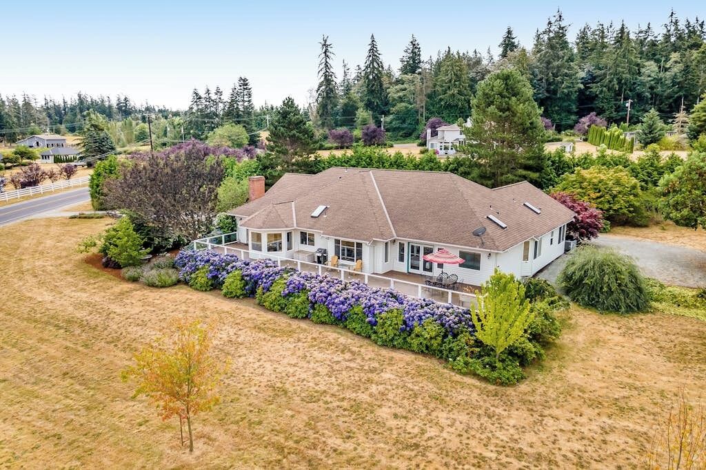 Ein eingeschossiges Haus mit überdachter Veranda, umgeben von einem gepflegten Garten und einem bewaldeten Hinterland.