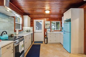 A compact kitchen with wooden ceiling, a stove, a sink, and a refrigerator. - Gorgeous 1BR - Patio - Firepit - Washer Dryer (Camano Island)