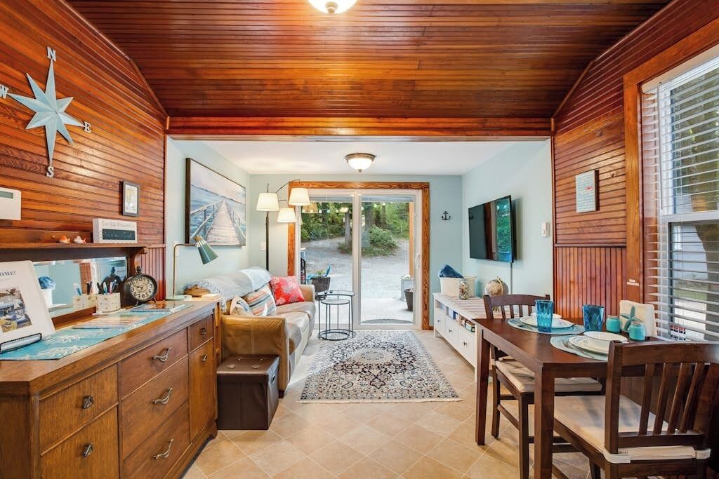 A cozy interior with a wooden ceiling, a dining area with a table and chairs, a sofa, and a rug.