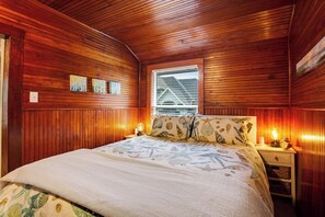 A bedroom with wooden paneling, a bed with a patterned bedspread, two bedside lamps, and a window with blinds. - Gorgeous 1BR - Patio - Firepit - Washer Dryer (Camano Island)
