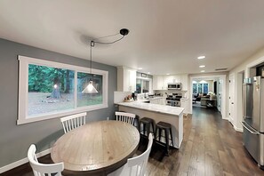 Ett modernt kök med en central köksö, vita skåp och ett stort fönster med utsikt över grönområden.