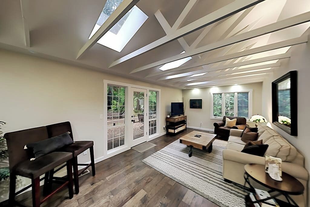 Sala de estar con sofá, mesa de centro y televisor. Hay puertas corredizas de vidrio que dan a un área exterior.