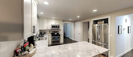 A modern kitchen with a marble countertop, stainless steel appliances, and a central island.