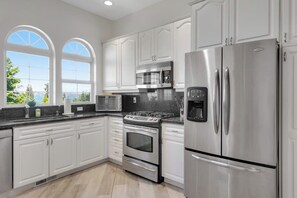 A modern kitchen with white cabinets, stainless steel appliances, and a view through large windows. - 3BR water-view home with fireplace, deck, tub, Washer Dryer (Blaine)