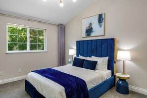 A bedroom with a large bed, a window with a view of trees, and a painting on the wall. - 3BR water-view home with fireplace, deck, tub, Washer Dryer (Blaine)