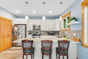 A kitchen with white cabinets, a stainless steel refrigerator, a microwave, and a large island with bar stools. - Amazing 2BR Soundview - Deck - Washer Dryer (Kingston)