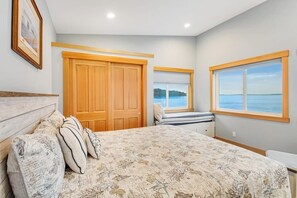 A bedroom with a bed, a window with a view of the sea, a wooden wardrobe, and a framed picture on the wall. - Amazing 2BR Soundview - Deck - Washer Dryer (Kingston)