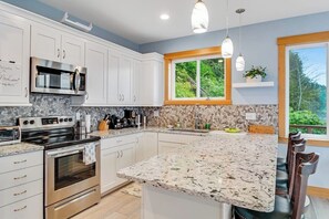 A modern kitchen with white cabinets, a granite countertop, stainless steel appliances, and a window with a view of greenery. - Amazing 2BR Soundview - Deck - Washer Dryer (Kingston)