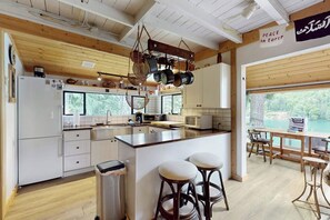 Une cuisine moderne avec des poutres en bois, un îlot central, des tabourets de bar et une vue sur un lac.