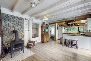 Ein rustikales Interieur mit einer Steinwand, einem Kaminofen, einer Küchenzeile mit Barhocker und einer Holzbalkendecke.