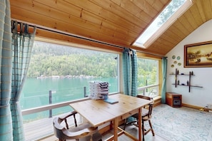 Une pièce avec une table en bois, des chaises, une vue sur un lac et un tableau accroché au mur.