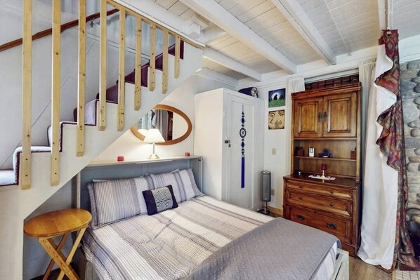 Una camera da letto con un letto, una cassettiera in legno, uno specchio, una lampada e una scala.
