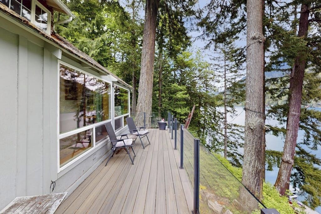 A deck with chairs and a table, overlooking a forested area and a body of water.