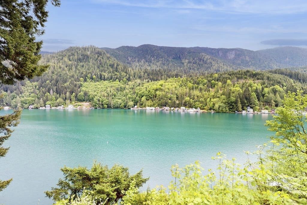 Ein See, umgeben von bewaldeten Hügeln unter blauem Himmel.