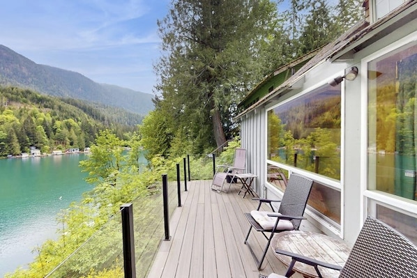 Une terrasse en bois avec des sièges extérieurs, offrant une vue sur un lac et des montagnes boisées.