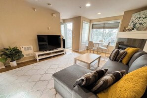 A living room with a sofa, a coffee table, a television, and a fireplace. - Corner 3BR - Fireplace - Balcony - Washer Dryer (Seattle)